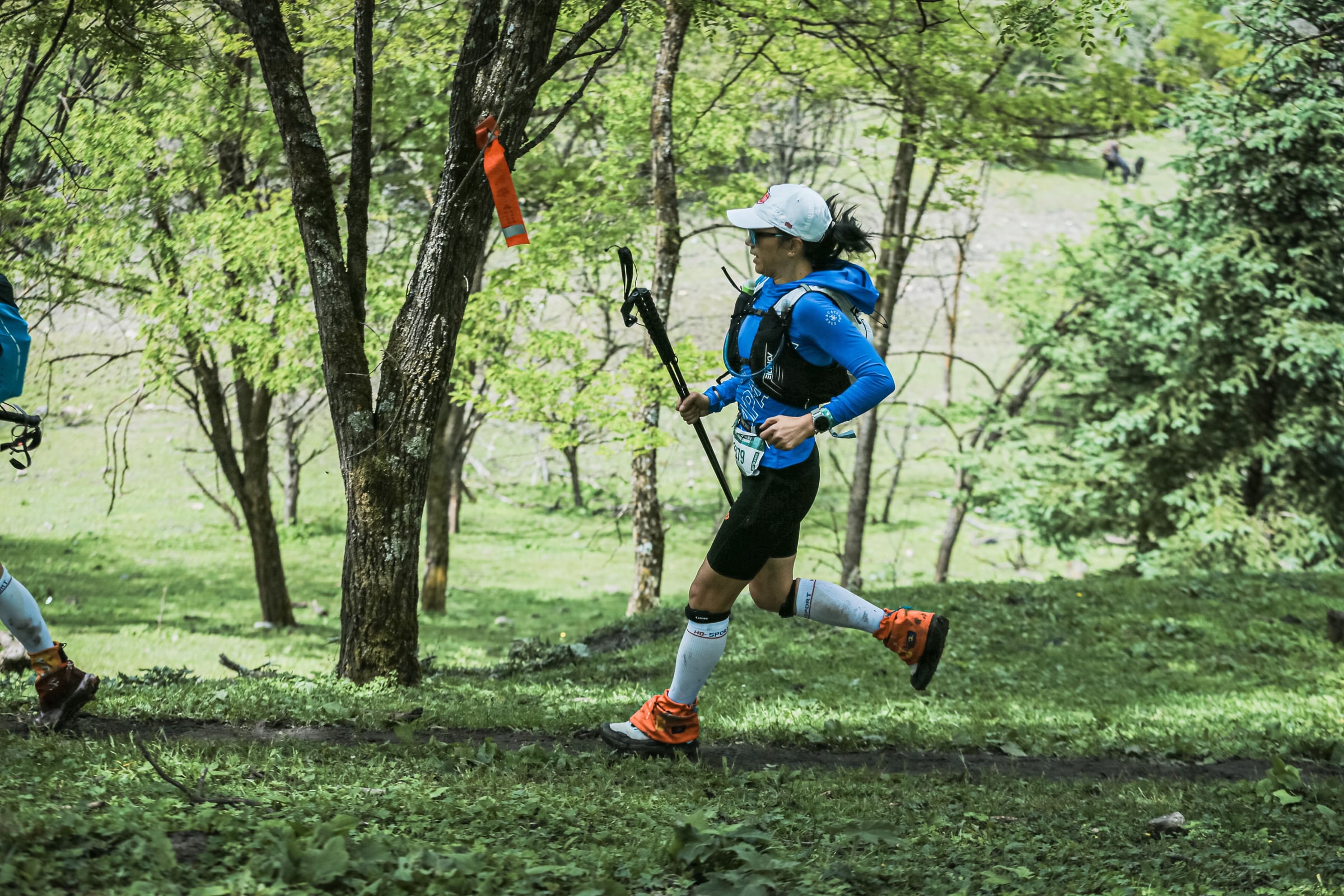 Trail runner with poles racing along a wooded path